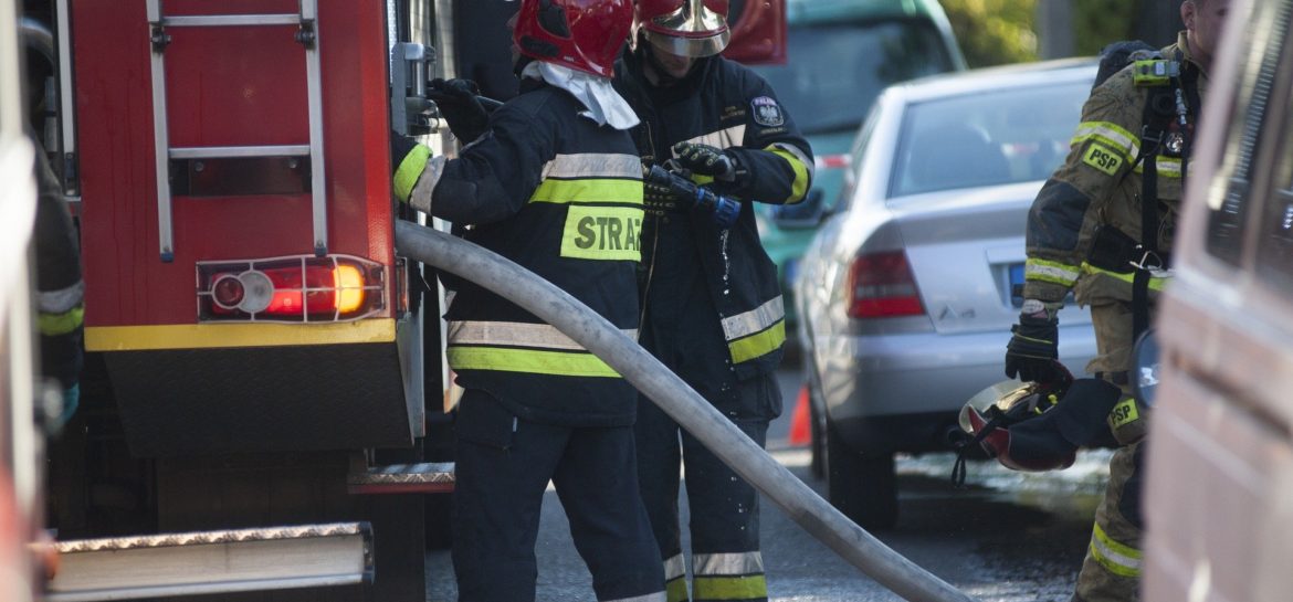 Dwóch strażaków PSP wyciąga węża strażackiego z pojazdu